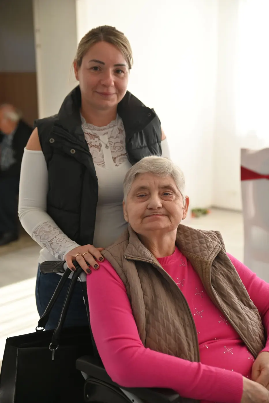 A carer standing with a smiling older woman in a wheelchair