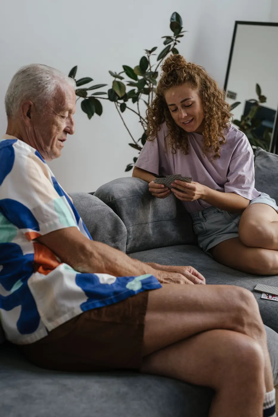 An older man playing cards with a carer on the sofa